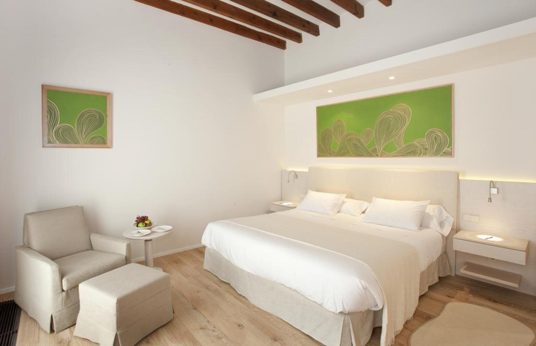 Ein Schlafzimmer mit einem Bett, einem Sessel, einem Nachttisch und einem an der Wand hängenden Kunstwerk.