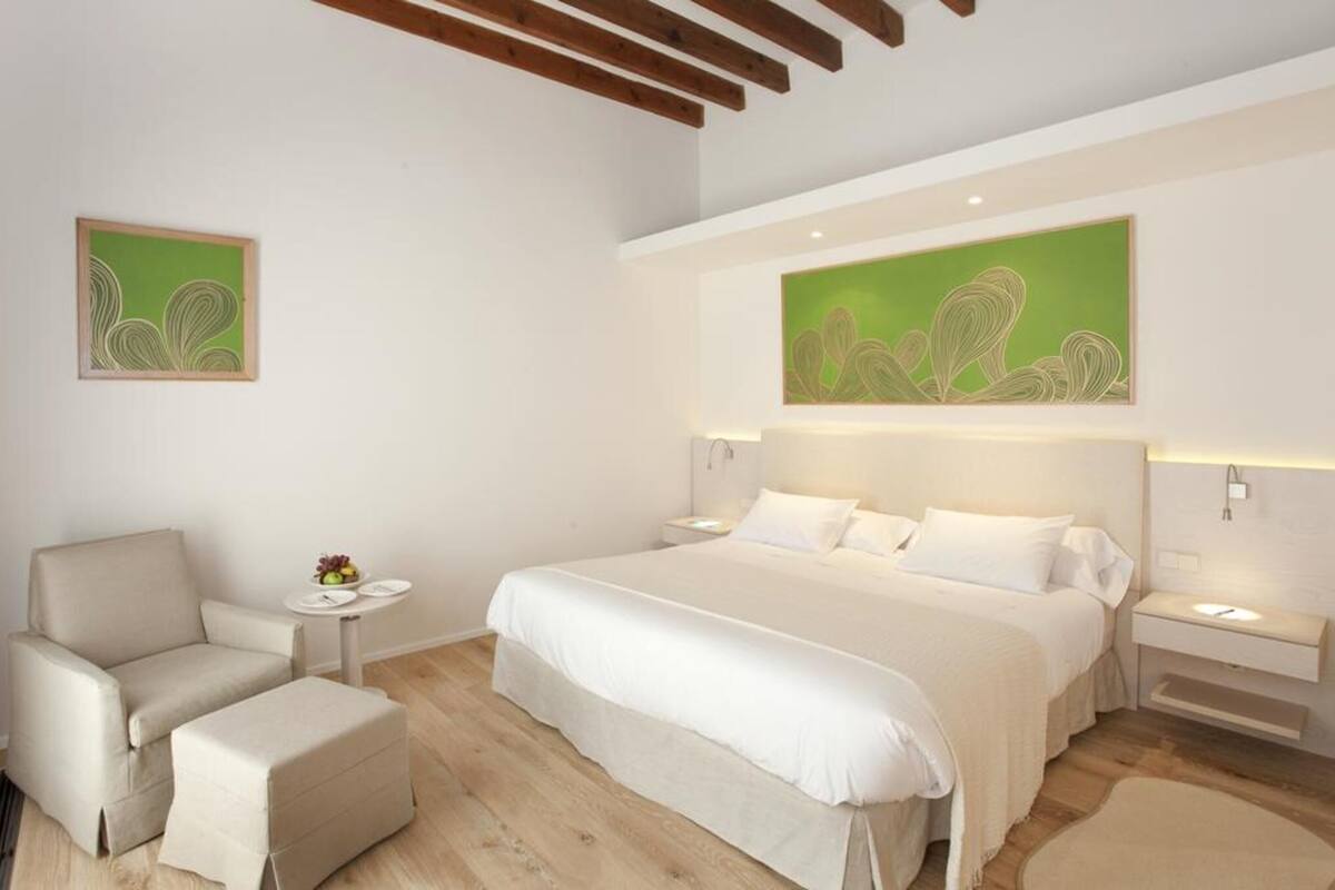 A bedroom with a bed, a chair, a bedside table, and a wall-mounted artwork.
