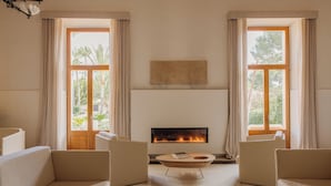 A living room with a fireplace, two sofas, a coffee table, and large windows with curtains. - Hotel Fontsanta Thermal Spa & Wellness, adults only – Preferred Hotels & Resorts (Campos)
