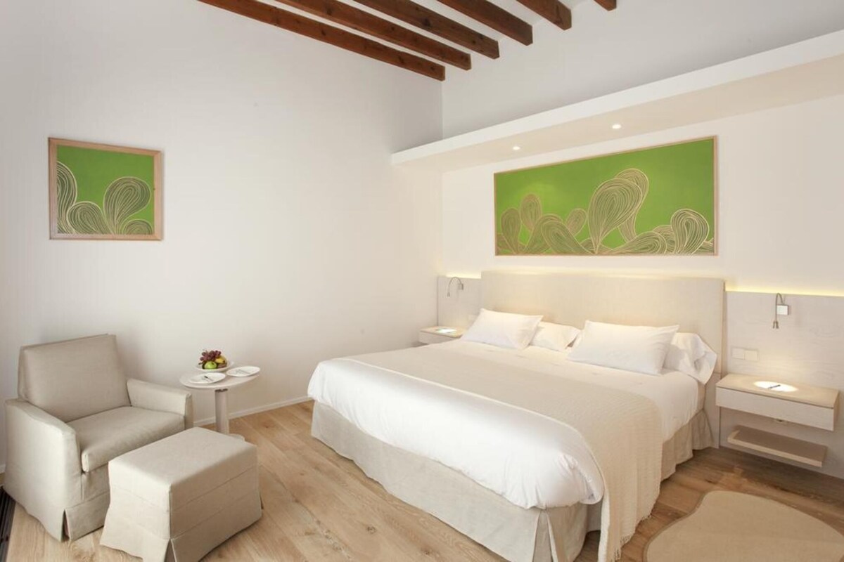 Une chambre à coucher comprenant un lit, une chaise, une table de chevet et une œuvre d’art accrochée au mur.