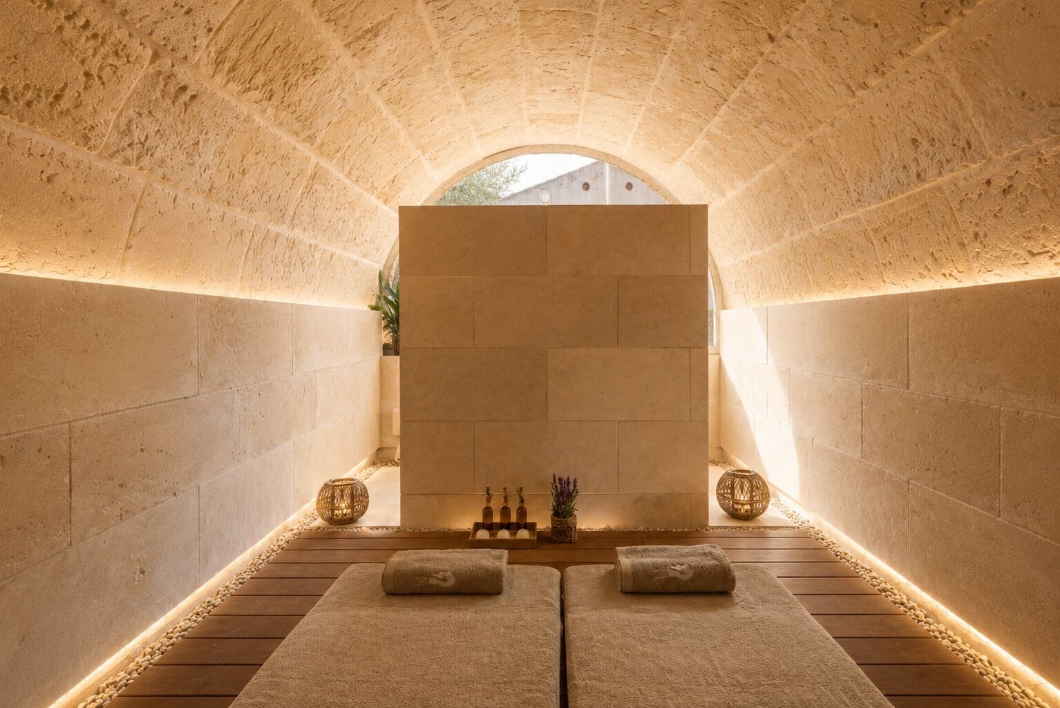 A spa room with stone walls, a wooden floor, and two massage tables.