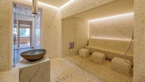 Un moderno espacio de spa con una pared de textura de piedra, un recipiente grande sobre un pedestal y una zona de estar con fuente de agua.