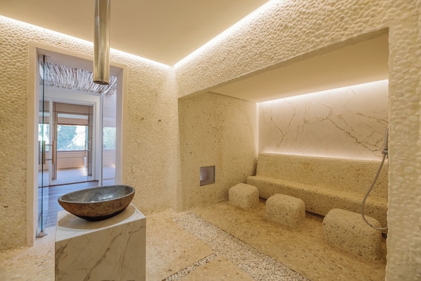 A modern spa area with a stone-textured wall, a large bowl on a pedestal, and a seating area with a water feature. - Hotel Fontsanta Thermal Spa & Wellness, adults only – Preferred Hotels & Resorts (Campos)