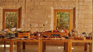 Un bufé de desayuno con diversos alimentos y un menú en una pizarra, en una sala con paredes de ladrillo visto y ventanas grandes.
