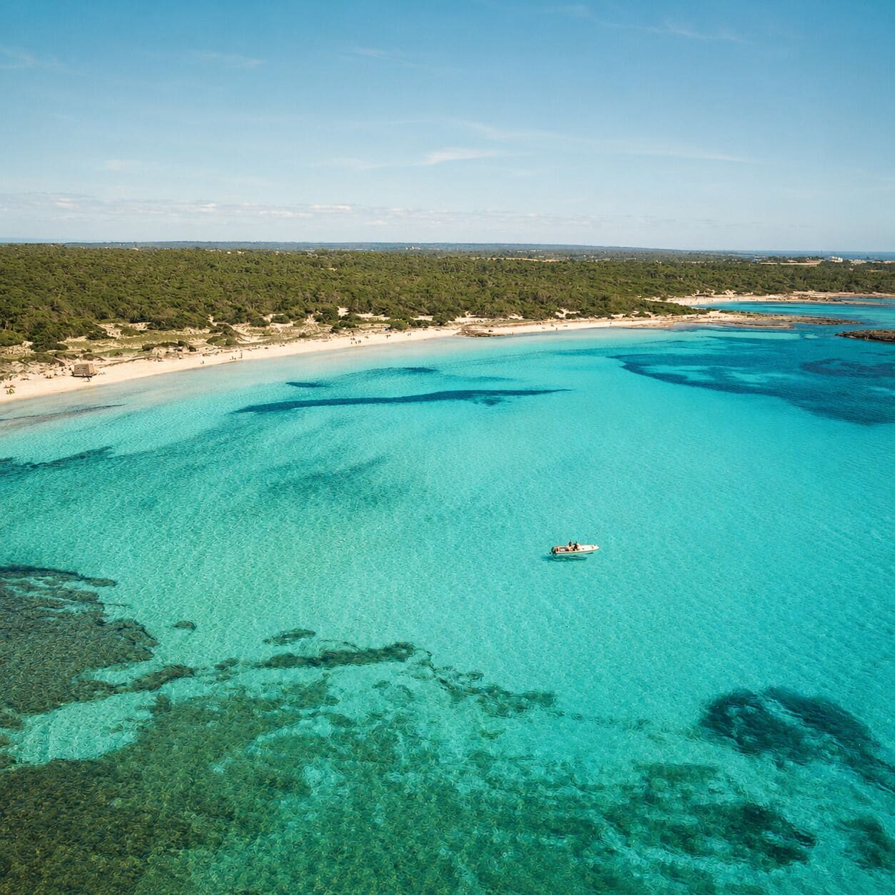 A coastal landscape with clear turquoise waters, a boat, and a beach area.