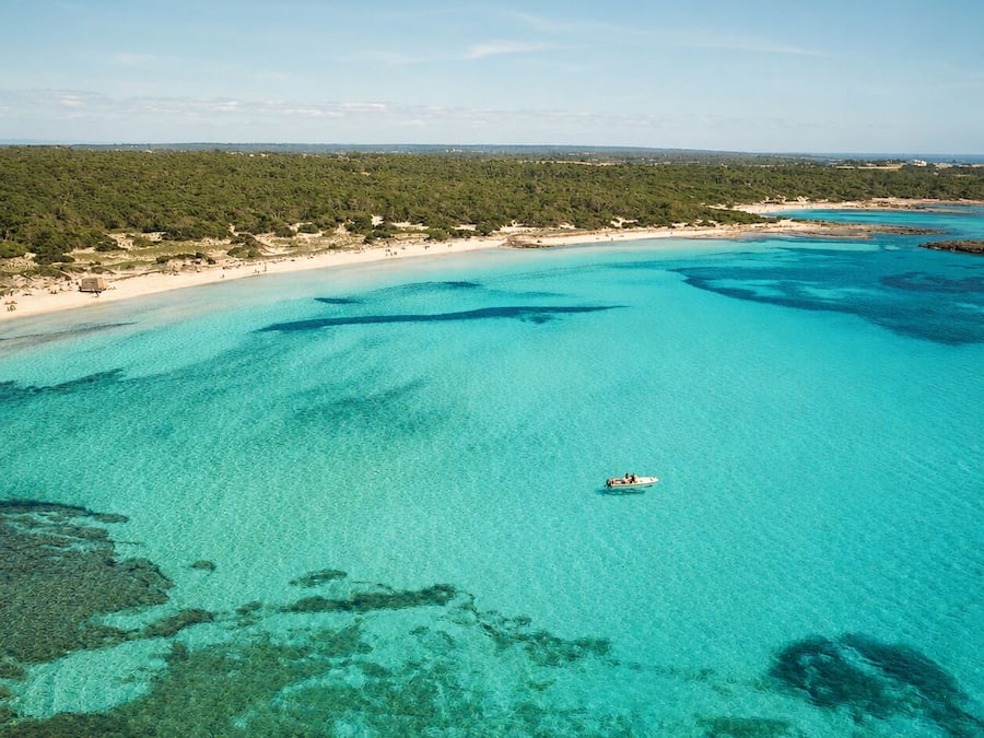A coastal landscape with clear turquoise waters, a boat, and a beach area.