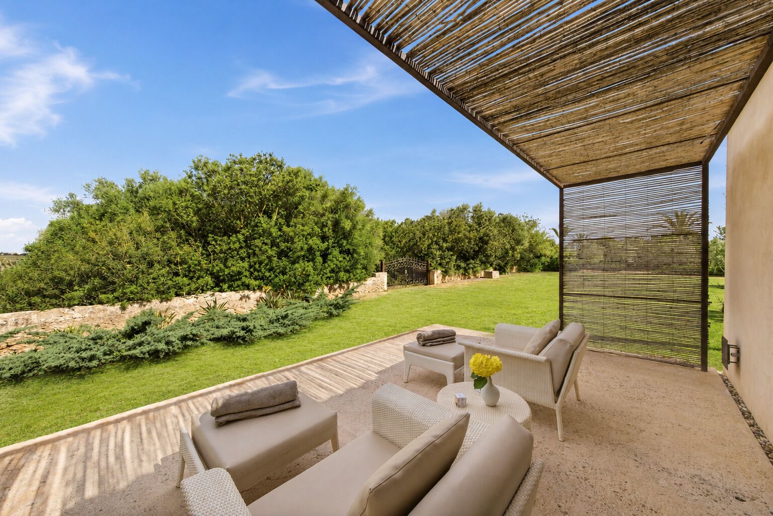 An outdoor patio with a seating area, a pergola, and a view of a landscaped garden.