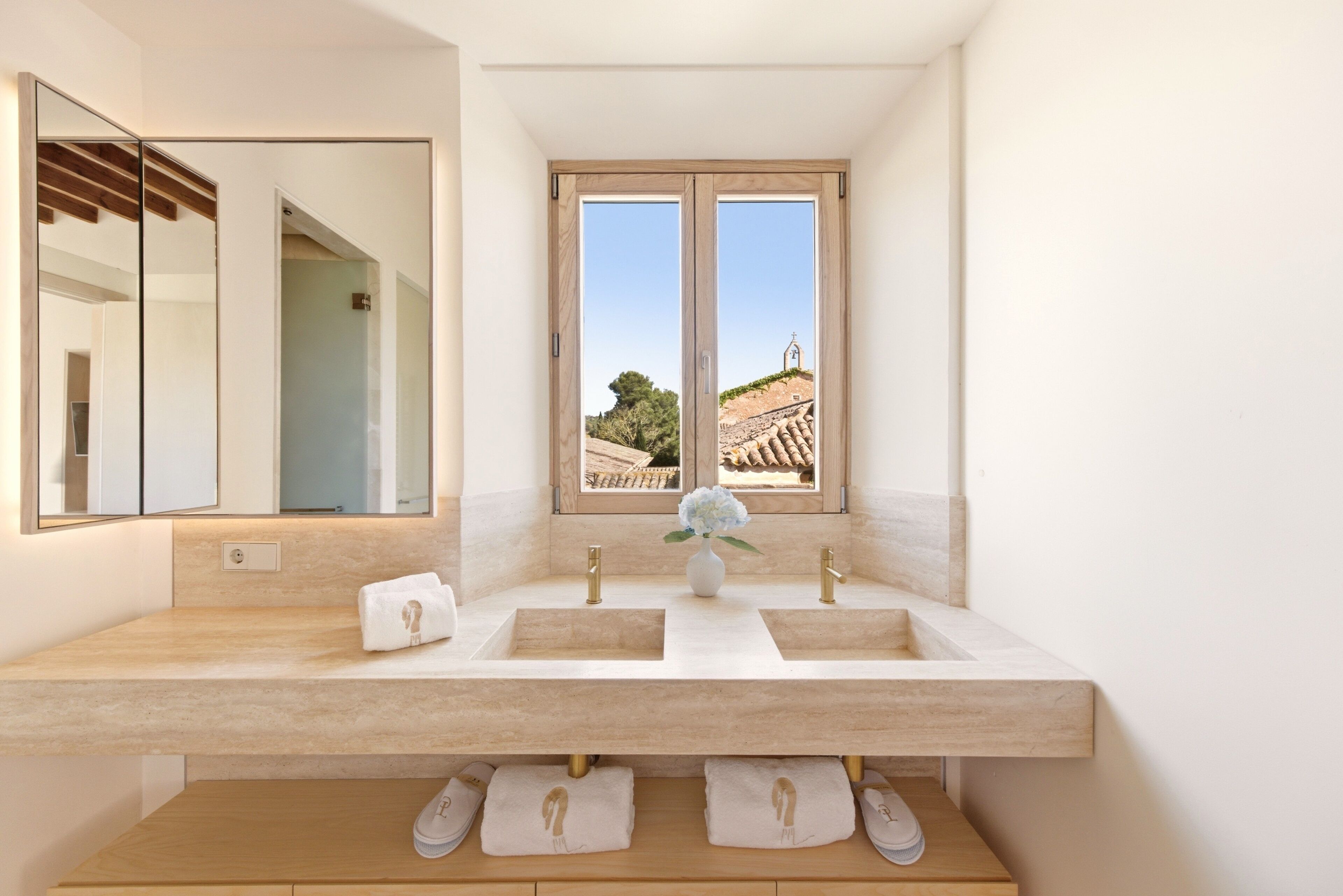 A bathroom with a double sink, a large mirror, and a window with a view of a building and trees.