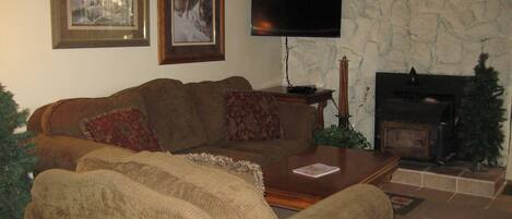 A living room with a brown sofa, a flat-screen TV, a fireplace, and framed pictures on the wall.