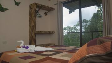 A bedroom with a large window, a quilted bedspread, and a towel with a swan design on the bed.