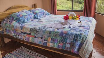 Uma cama com um edredom colorido, uma toalha branca e um buquê de flores.