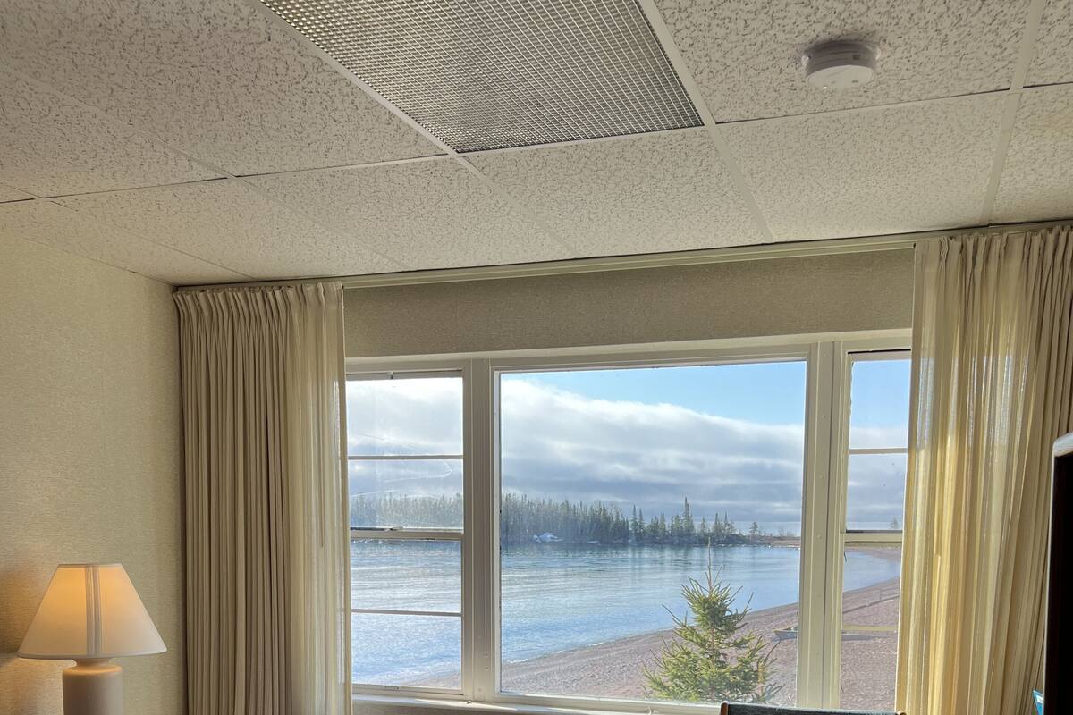 A hotel room with a large bed, a chair, a desk, and a window with a view of a lake and forest.