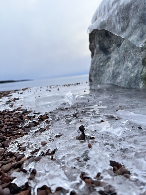 A close-up of a rocky beach with clear water and ice formations.