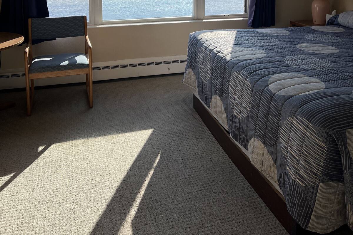 A bedroom with a large window, a bed, a chair, and a nightstand.