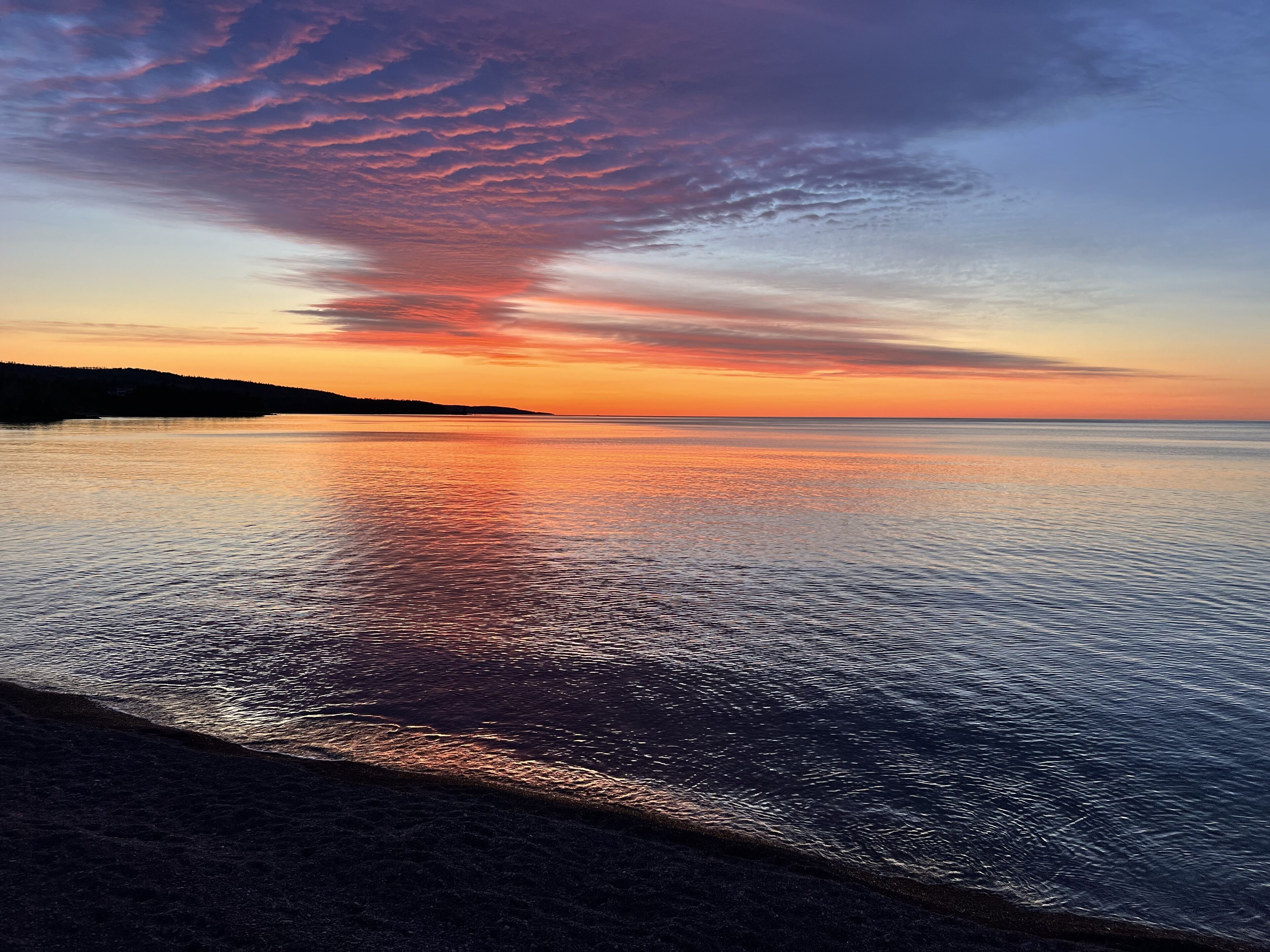Un atardecer sobre un mar tranquilo, con una playa al frente.
