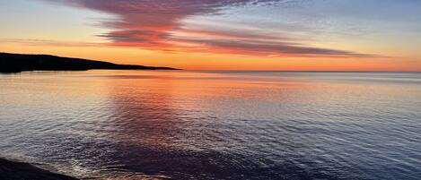 Un atardecer sobre un mar tranquilo, con una playa al frente.