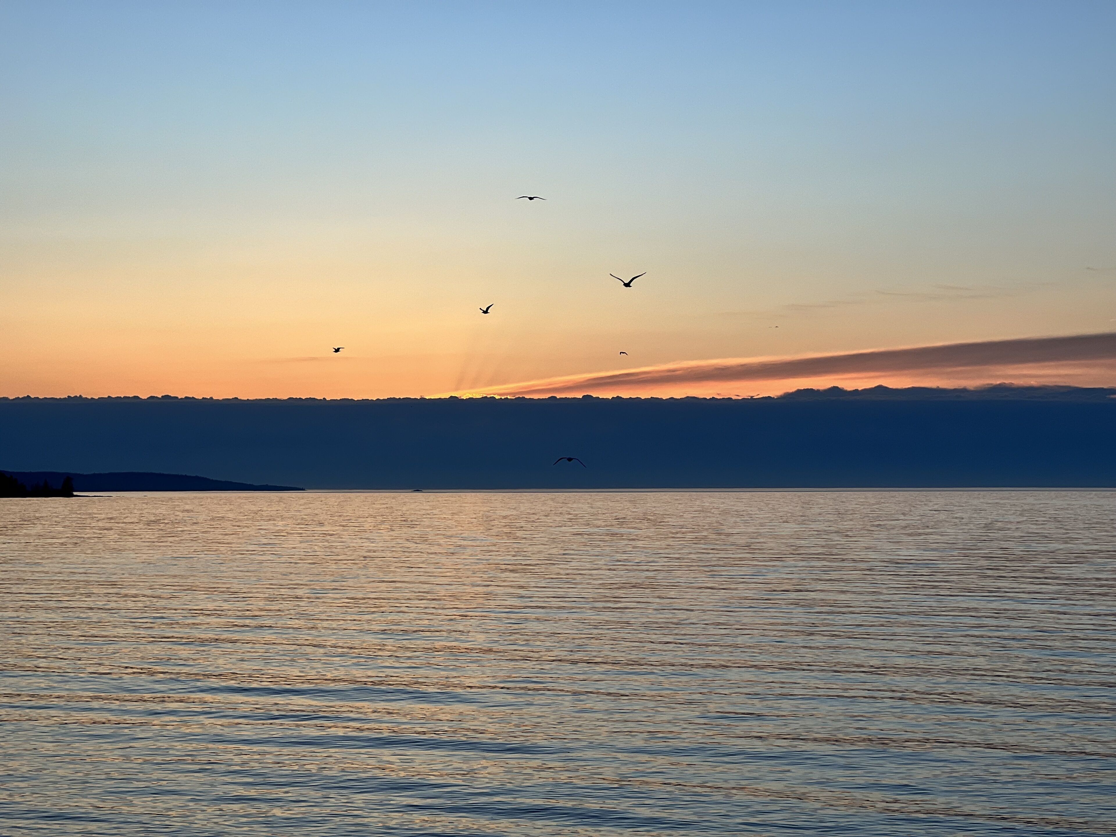 A sunset over a calm body of water with silhouettes of mountains in the distance.