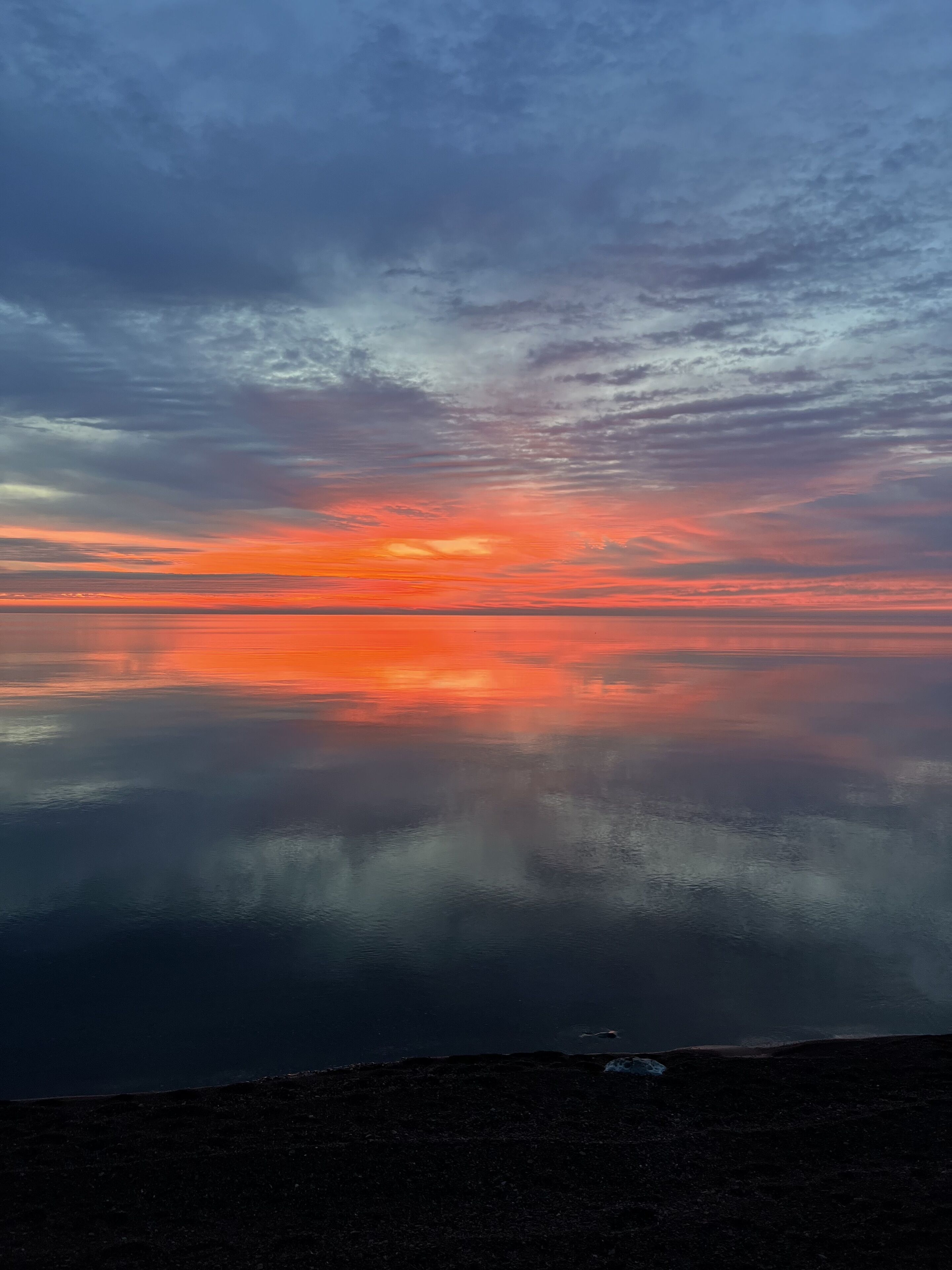 Un cuerpo de agua tranquila reflejando un cielo de atardecer con nubes.