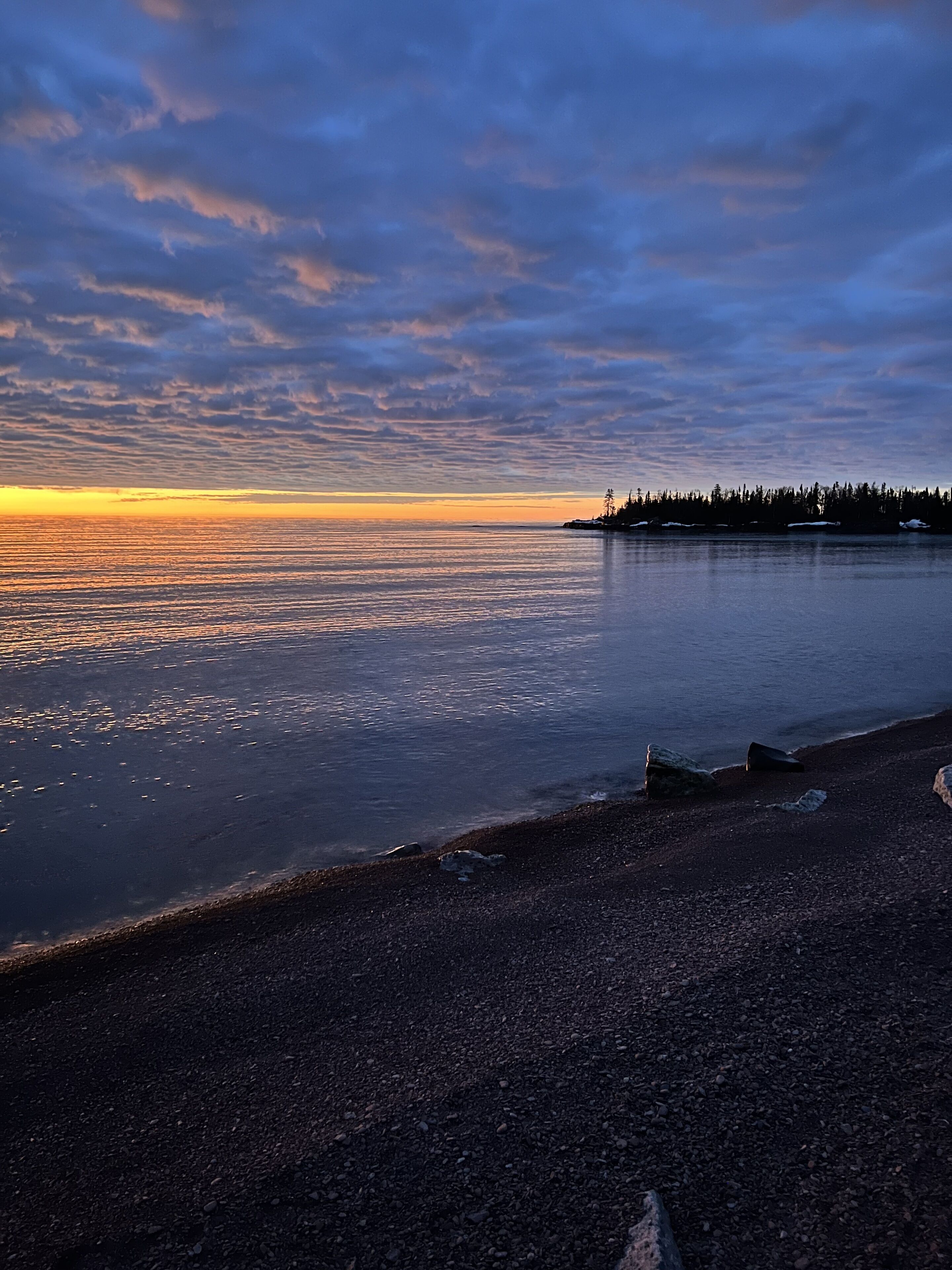 A beach with a rocky shoreline and a forested island in the distance.