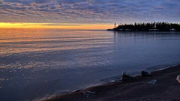 A beach with a rocky shoreline and a forested island in the distance.