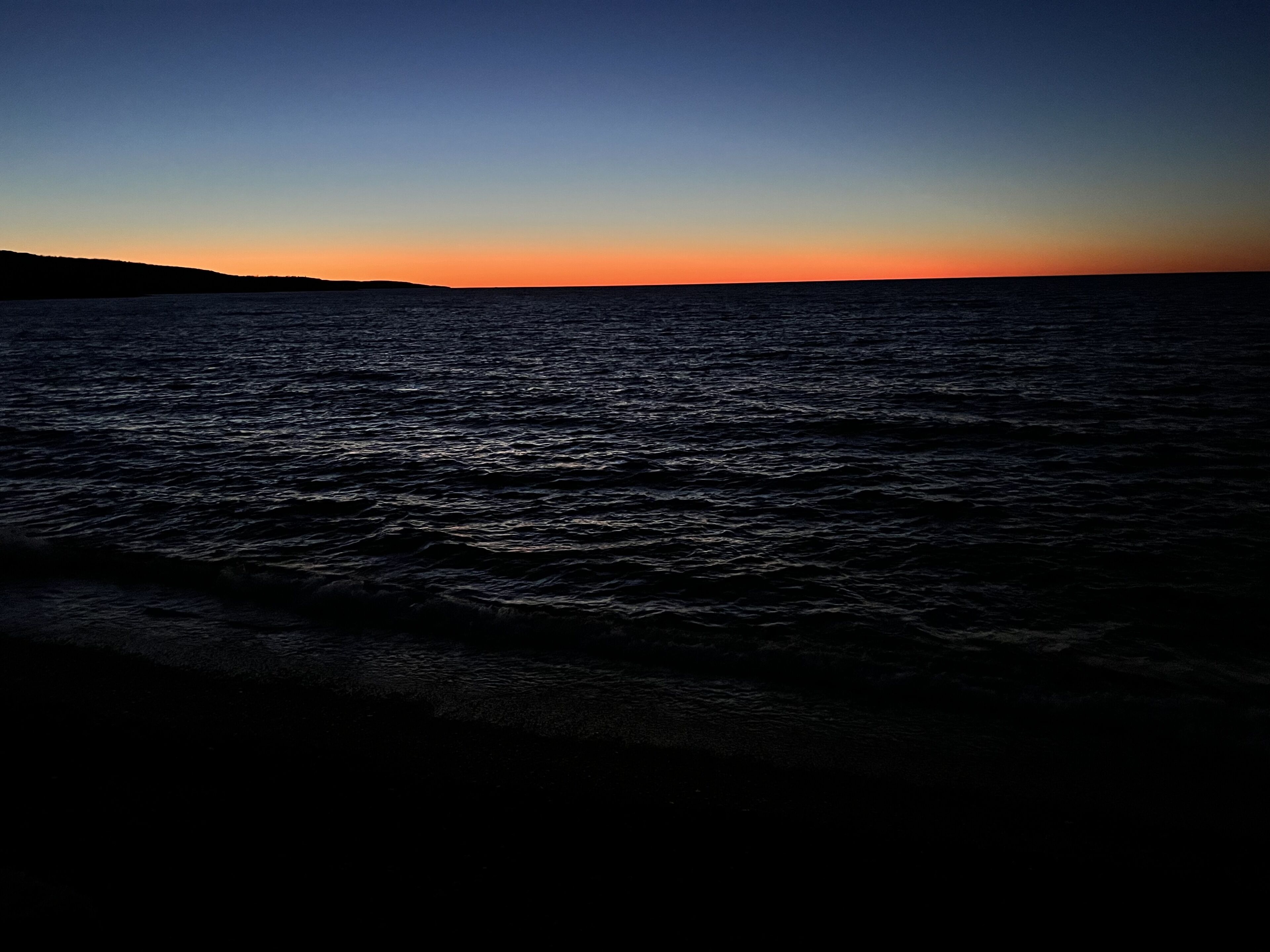 A calm sea at sunset with a clear sky.