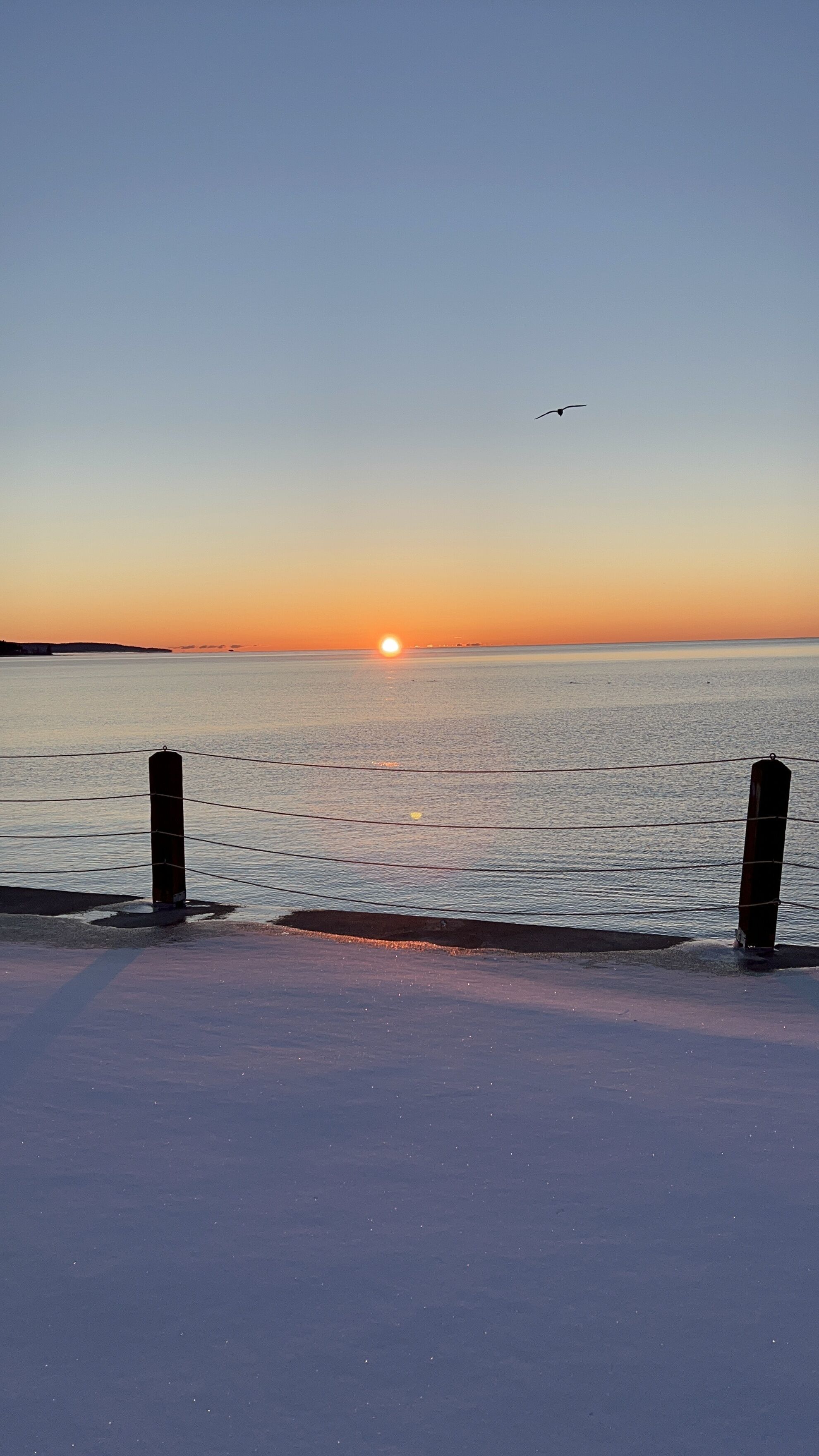 Un coucher de soleil sur une mer calme, avec une jetée au premier plan.