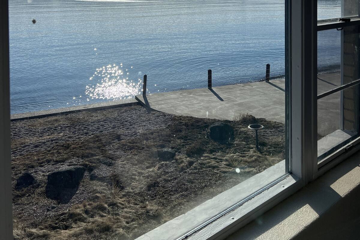 A view through a window of a body of water, a cloudy sky, and a concrete dock.