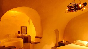 Une chambre dotée d’une grande baignoire, d’un lit et d’un petit coin salon. Un miroir est accroché au mur et un lustre se trouve au-dessus du lit.