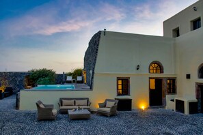 A modern building with a pool, outdoor seating, and a stone wall. - Santorini Heritage Villas & Mansions (Santorini)