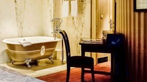 Un baño antiguo con una bañera independiente, una mesita pequeña y una silla.