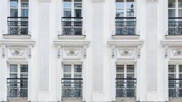 Fachada de edificio con columnas blancas y marcos de ventanas ornamentados.