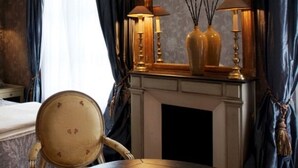 Una habitación con chimenea, una silla de madera y dos lámparas sobre una repisa.