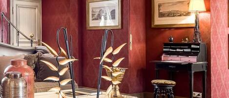 Um quarto com parede vermelha, um piano, uma mesa com objetos decorativos e uma luminária.