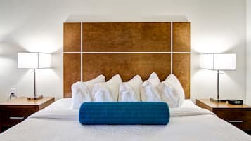 A neatly made bed with white linens, a blue accent pillow, and a wooden headboard. There are two bedside tables with lamps and a digital clock.