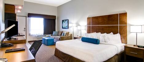 Una habitación de hotel con una cama grande, un escritorio con computadora, una silla, un sofá y una mesita de noche con lámpara.