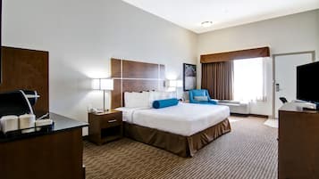 A hotel room with a large bed, a desk with a computer, a chair, a TV, and a window with curtains.