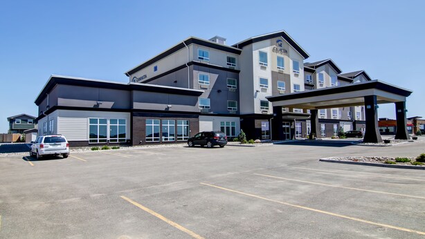 A multi-story hotel with a modern design, featuring a covered entrance and a parking lot with several cars.