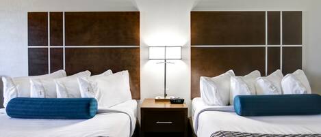 A hotel room with two beds, a nightstand, a lamp, and a clock.