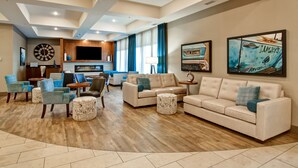 A spacious living area with a large sofa, armchairs, and a coffee table. There is a flat-screen TV mounted on the wall, and artwork is displayed on the walls.