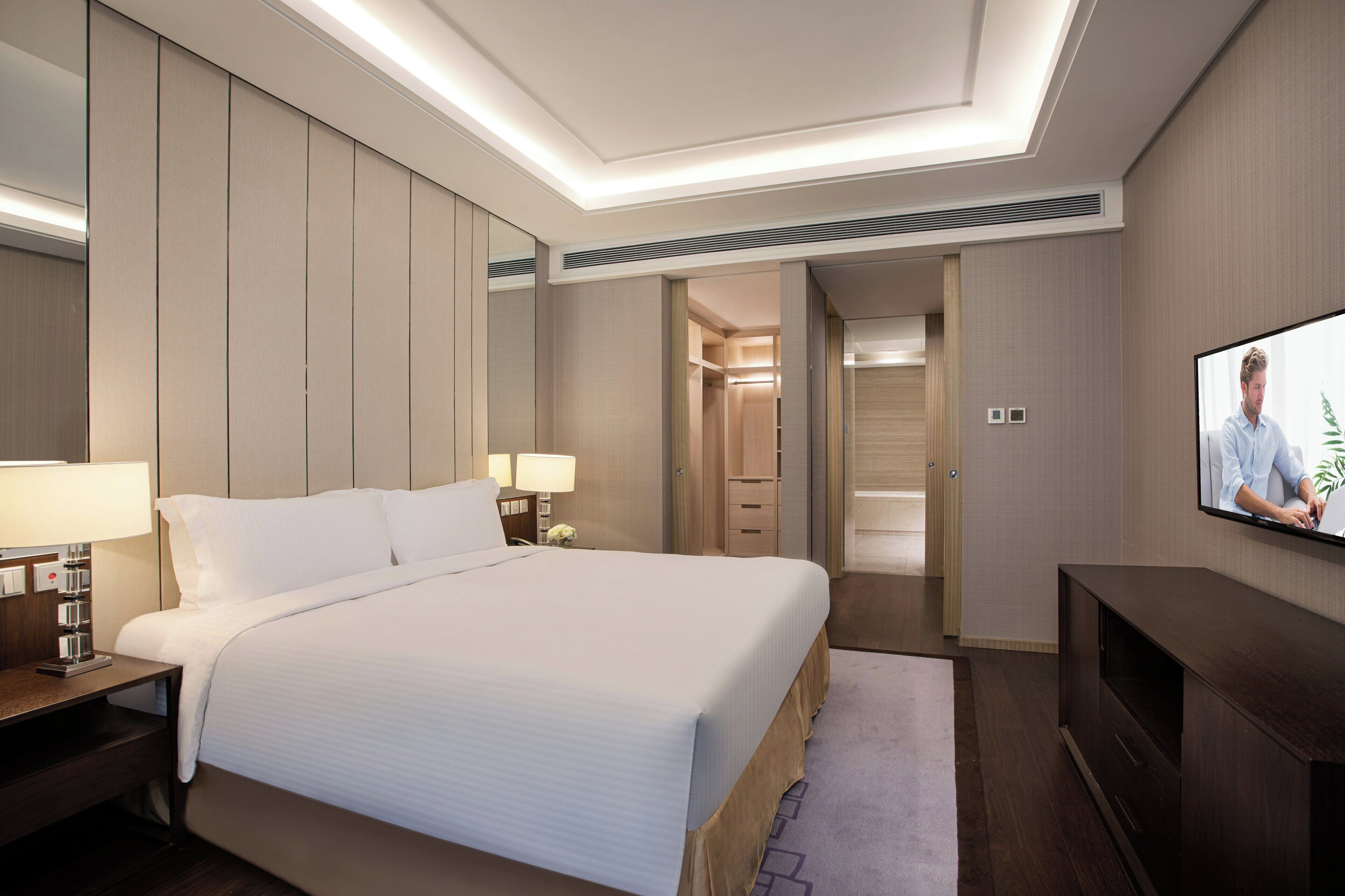 A hotel room with a large bed, bedside lamps, a TV, and a walk-in closet.