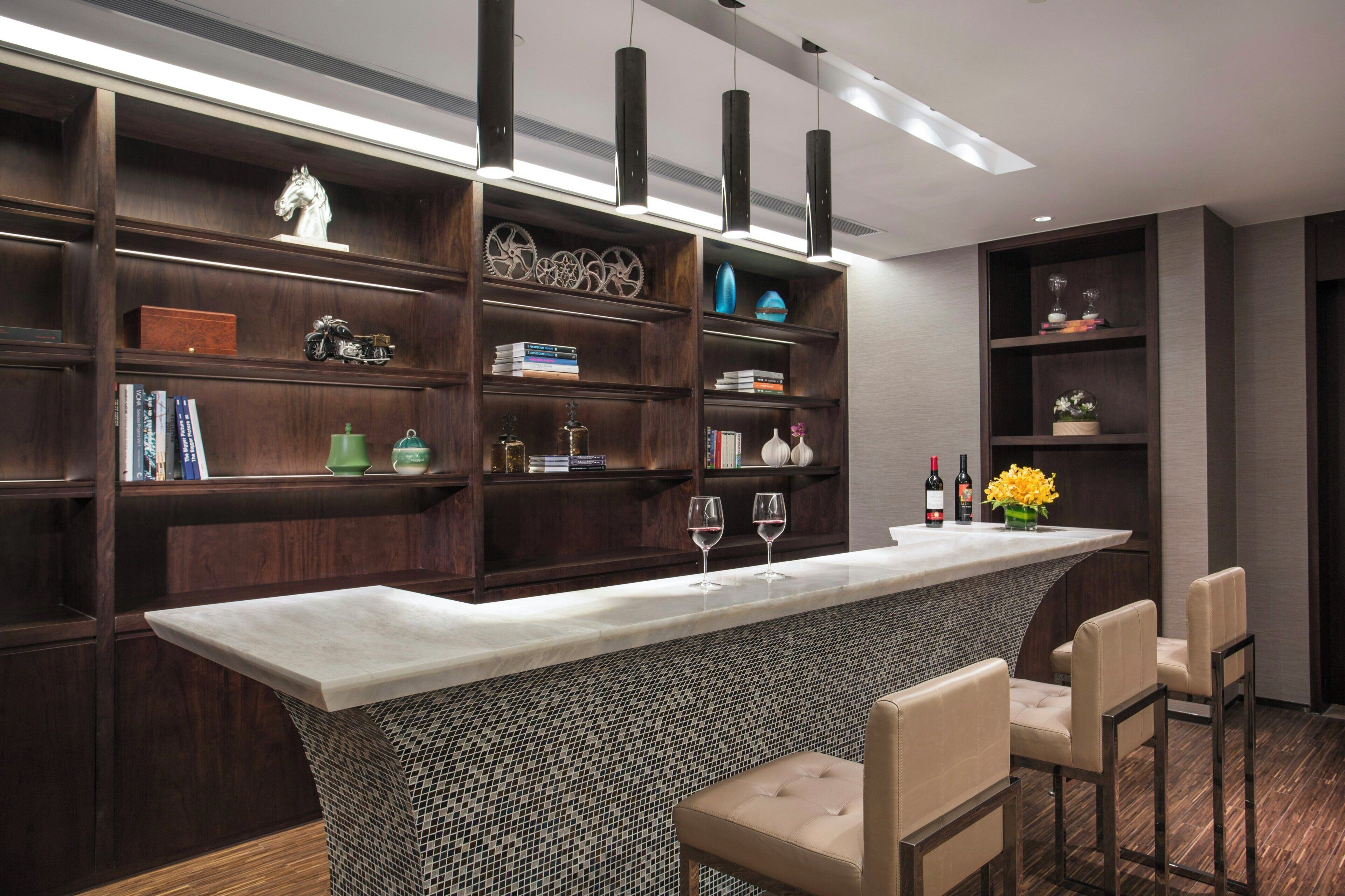 A modern bar area with a marble countertop, two bar stools, and a variety of decorative items on shelves.