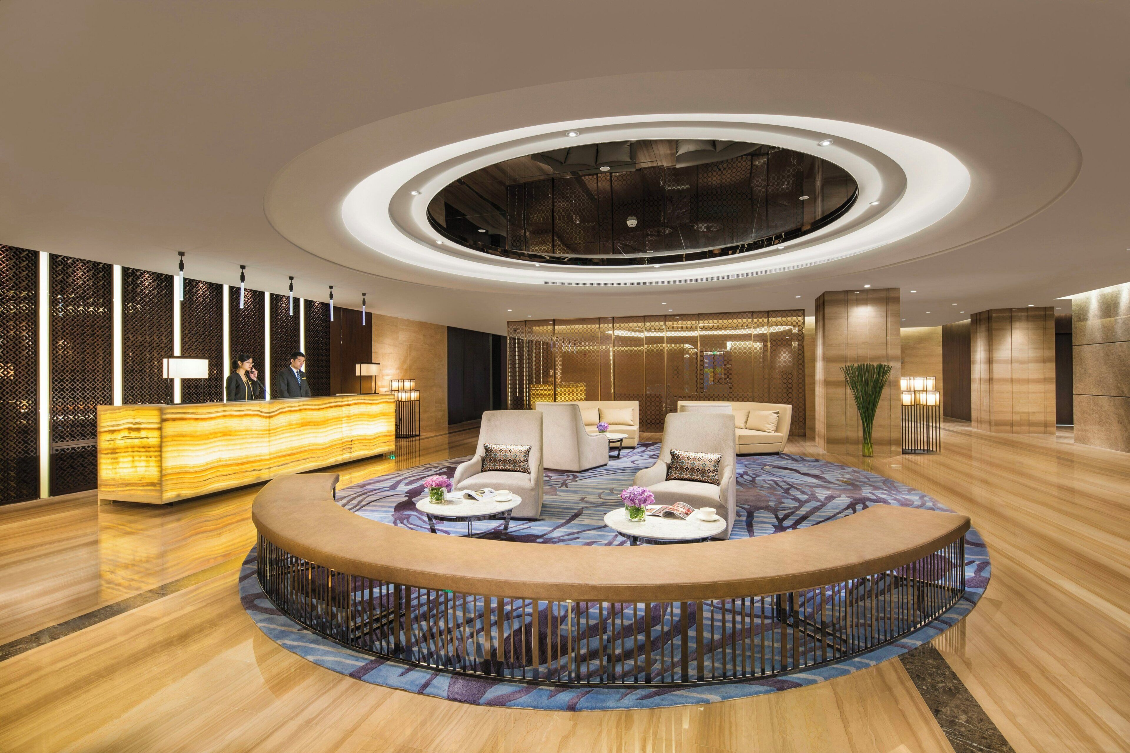 A hotel lobby with a reception desk, seating area, and a circular decorative feature.