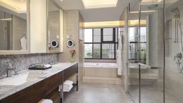 A modern bathroom with a large mirror, a vanity with a marble countertop, a bathtub, and a glass-enclosed shower area.