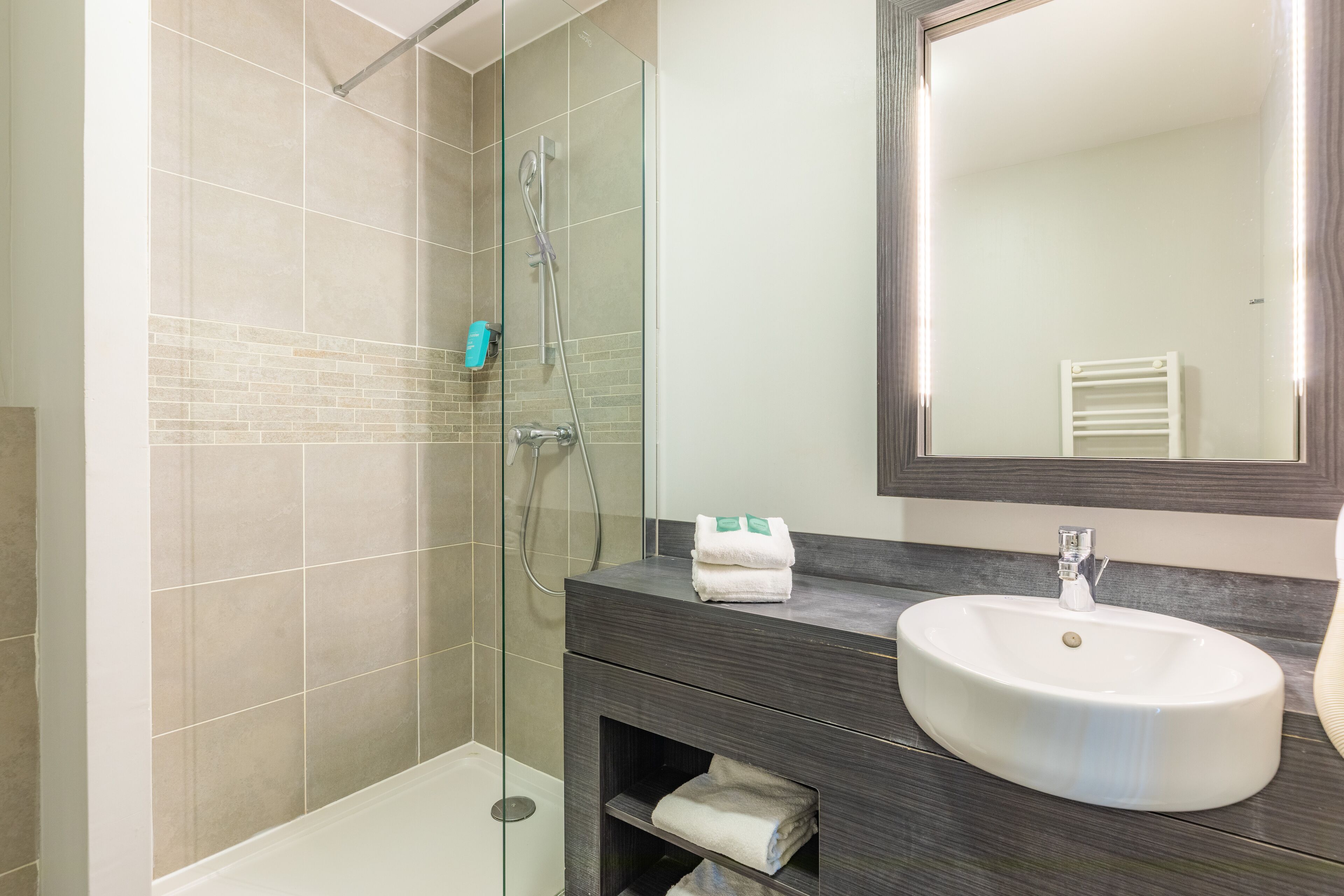 Un baño moderno con ducha de vidrio, un lavabo blanco y un mueble de tocador oscuro.