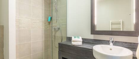 Un baño moderno con ducha de vidrio, un lavabo blanco y un mueble de tocador oscuro.
