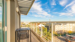 A balcony with a table and chairs, overlooking a cityscape with buildings and a clear sky. - Appart'City Confort Montpellier Ovalie 2 (Montpellier)