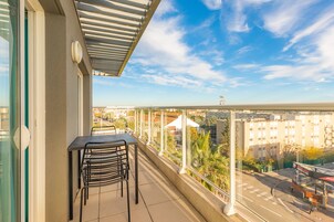 Un balcón con mesa y sillas, con vista a un paisaje urbano con edificios y cielo despejado.
