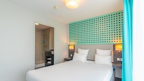 A hotel room with a large bed, a shower, a wall-mounted light fixture, and a headboard with a dot pattern. - Appart'City Confort Montpellier Ovalie 2 (Montpellier)