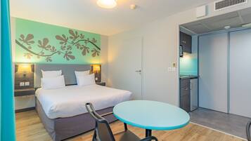 A hotel room with a bed, bedside tables, a round table, and a kitchenette.