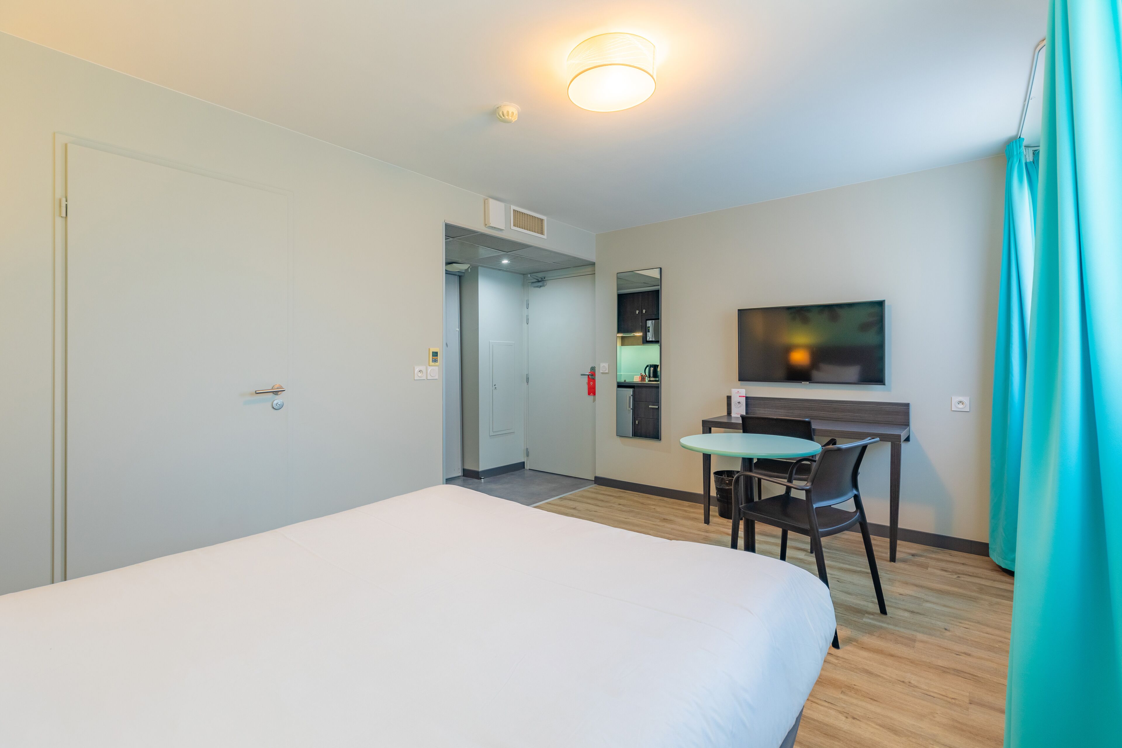 Une chambre d’hôtel équipée d’un lit, d’un bureau, d’une chaise, d’une télévision et d’une kitchenette.